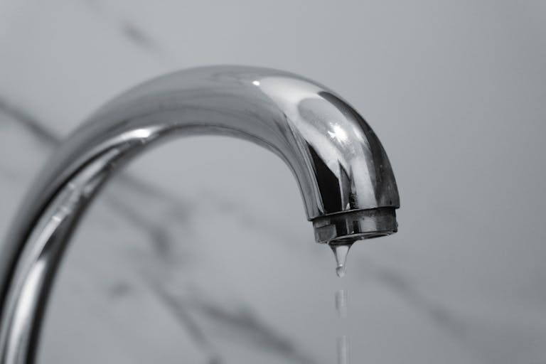 A close-up shot of a modern chrome bathroom faucet with water dripping from the tip.